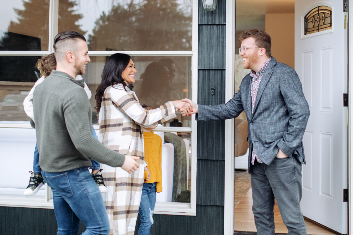 A couple with a child smiles while they shake hands, meeting a REALTOR® 
