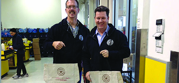 Town of Cochrane economic development officer Robert Kalinovich and economic development manager Mike Korman hand out Proudly Cochrane reusable shopping bags at a local grocery store. Photo courtesy Town of Cochrane.